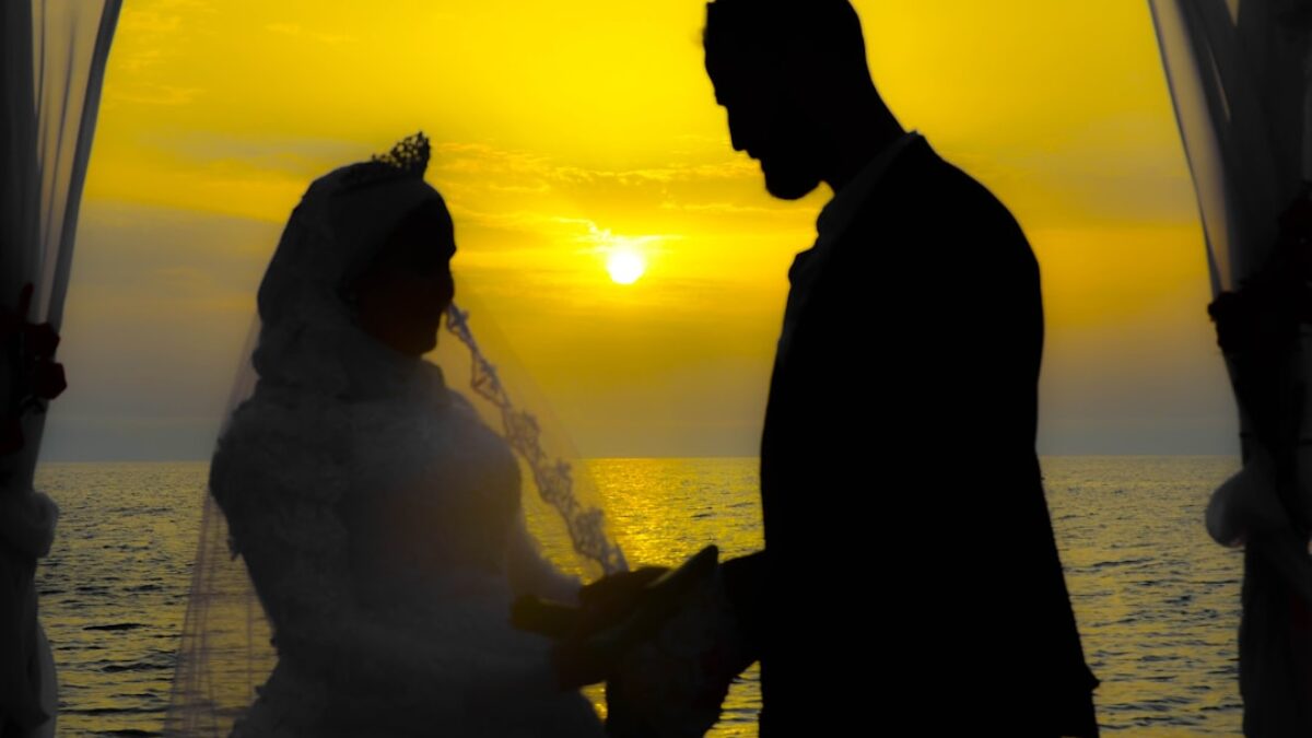 silhouette of man and woman standing near body of water during sunset