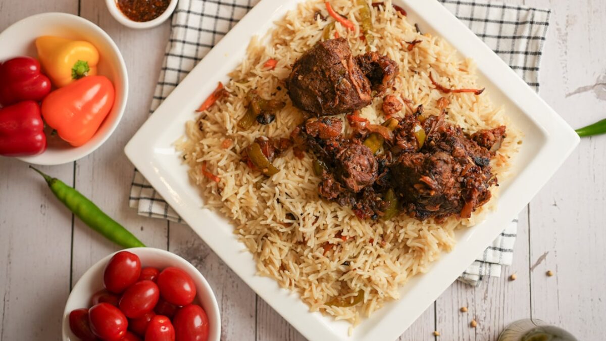 A white plate topped with meat and rice next to bowls of vegetables