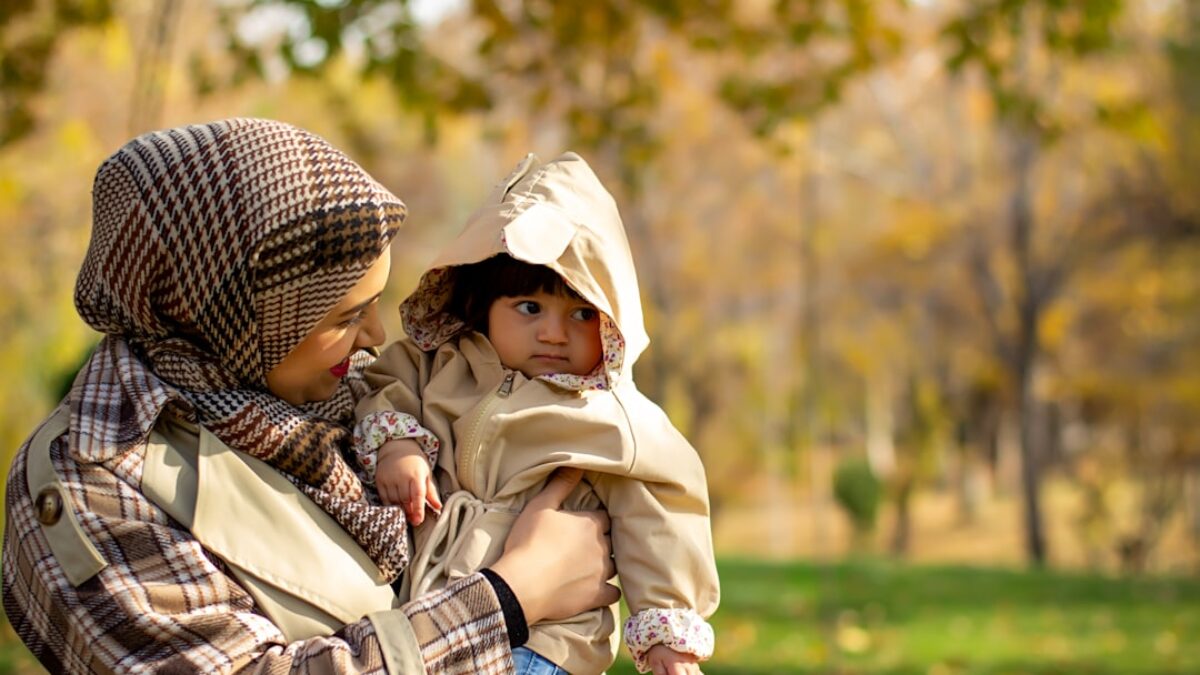Mother holds her child in a park during autumn.